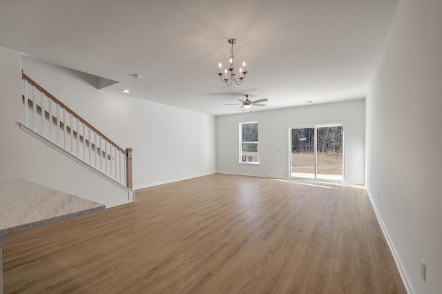 unfurnished living room with light wood-type flooring, stairs, baseboards, and ceiling fan with notable chandelier