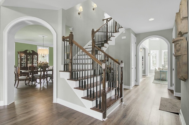 stairway with arched walkways, baseboards, and wood finished floors