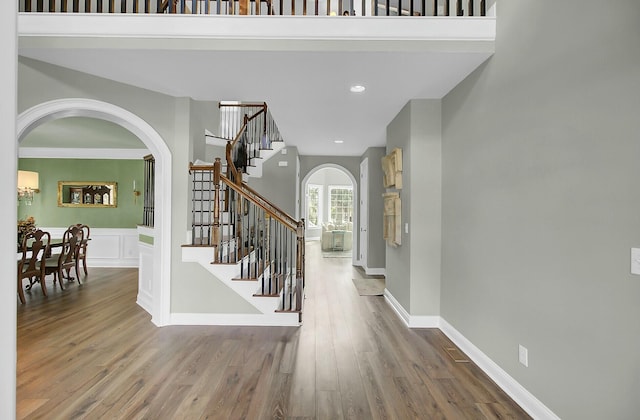 foyer entrance featuring baseboards, arched walkways, wood finished floors, stairs, and recessed lighting