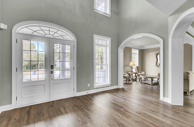 foyer entrance with a towering ceiling, baseboards, arched walkways, and wood finished floors