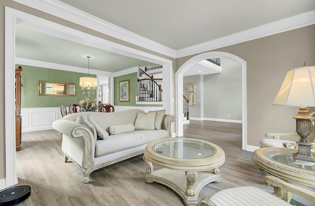 living area featuring arched walkways, stairway, wood finished floors, and crown molding