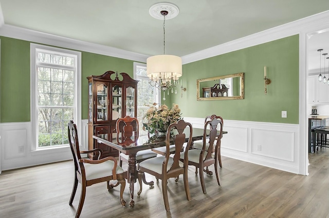 dining area with ornamental molding, a wainscoted wall, a notable chandelier, and wood finished floors