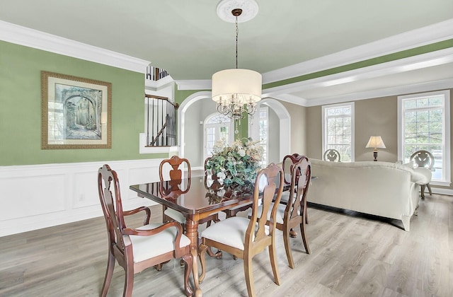 dining area featuring light wood finished floors, arched walkways, and crown molding