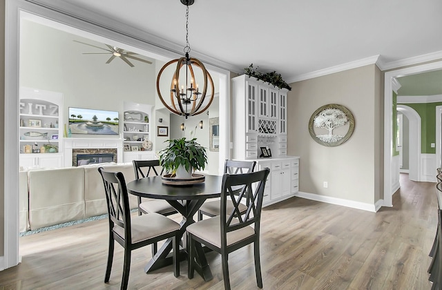 dining space with arched walkways, wood finished floors, crown molding, and a high end fireplace