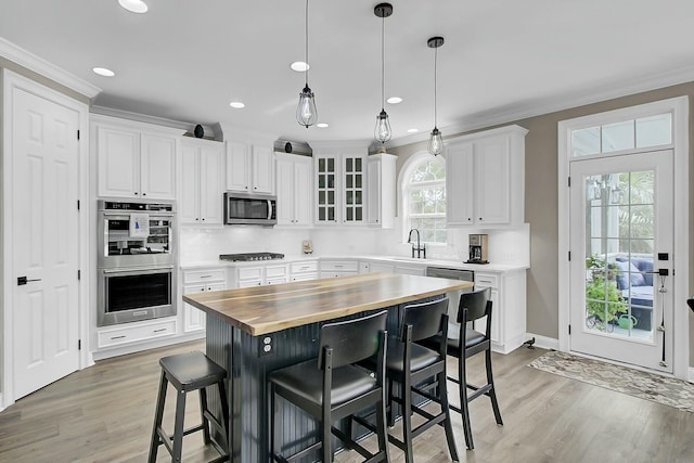 kitchen with white cabinetry, butcher block counters, appliances with stainless steel finishes, and a breakfast bar