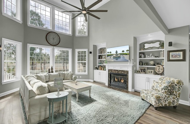 living area with built in shelves, baseboards, a premium fireplace, and wood finished floors