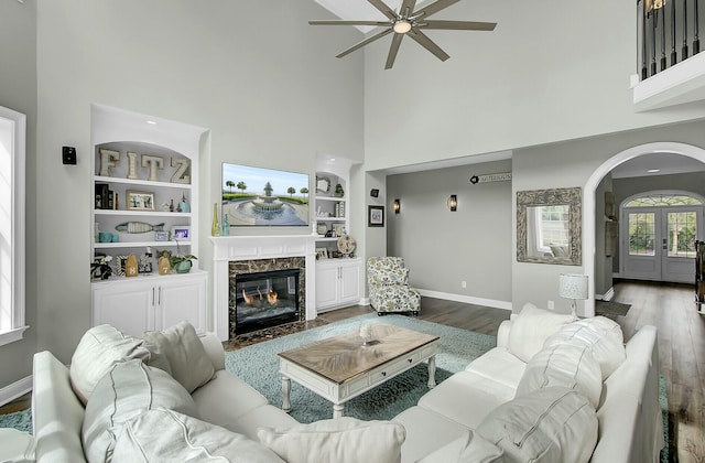 living room featuring baseboards, arched walkways, wood finished floors, built in shelves, and a fireplace