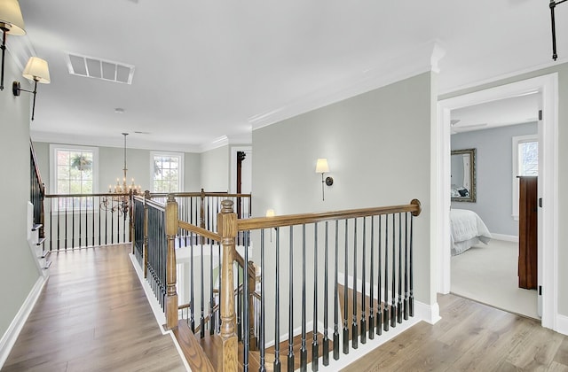 corridor featuring wood finished floors, an upstairs landing, visible vents, and an inviting chandelier