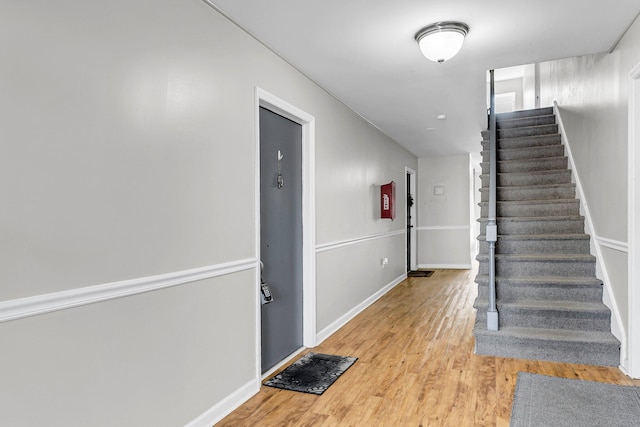 foyer entrance featuring light wood-style flooring, stairway, and baseboards