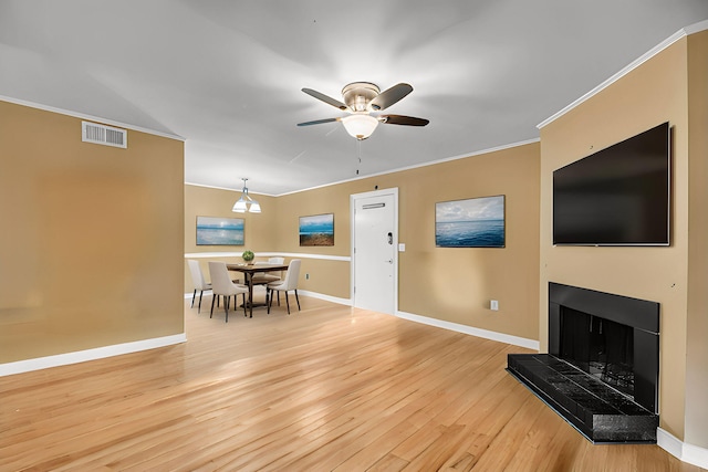 living area with a fireplace with raised hearth, light wood-style flooring, visible vents, baseboards, and crown molding