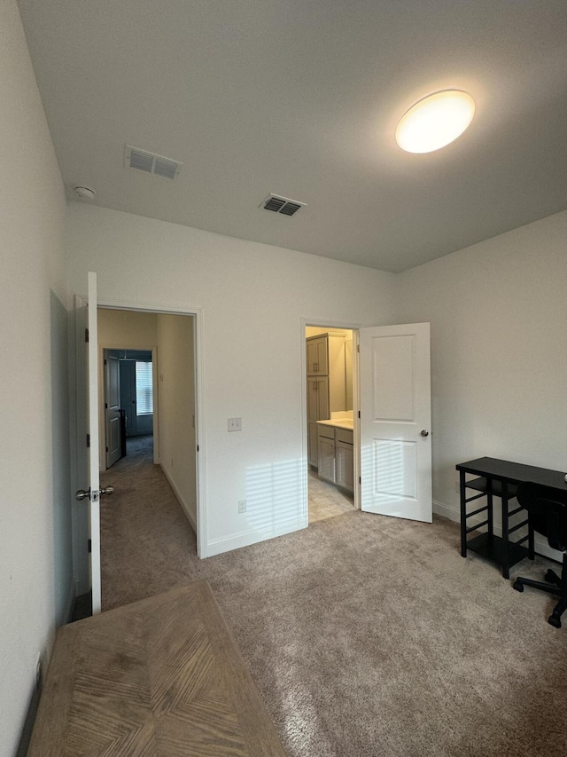 bedroom with light carpet, ensuite bathroom, visible vents, and baseboards