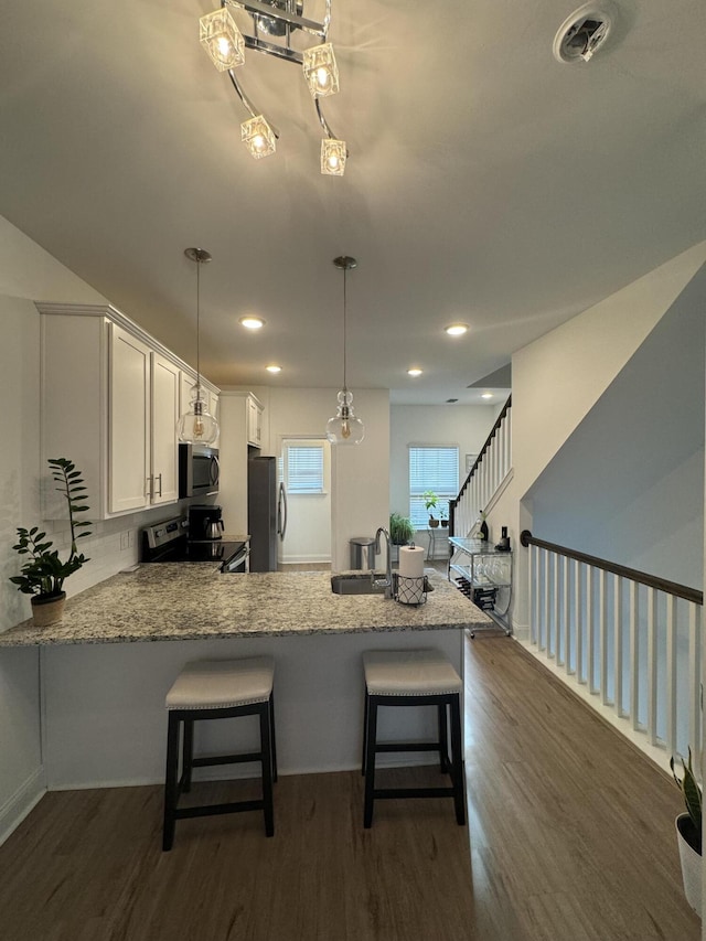 kitchen with white cabinets, dark wood-type flooring, a peninsula, stainless steel appliances, and a sink