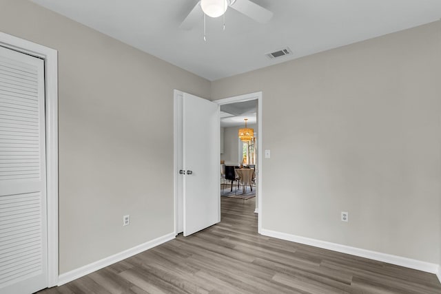 unfurnished bedroom with ceiling fan with notable chandelier, wood finished floors, visible vents, and baseboards