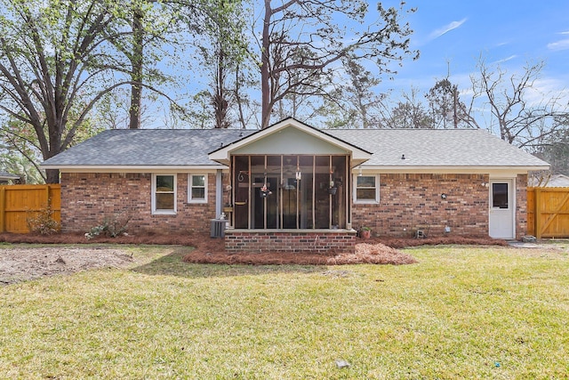 rear view of house featuring a lawn, fence, roof with shingles, a sunroom, and brick siding