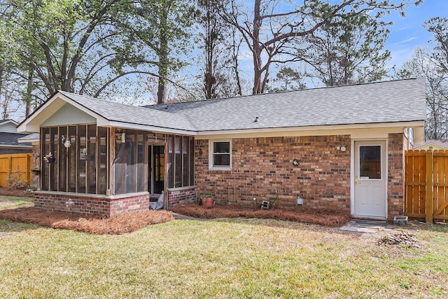 rear view of property featuring fence, roof with shingles, a yard, a sunroom, and brick siding