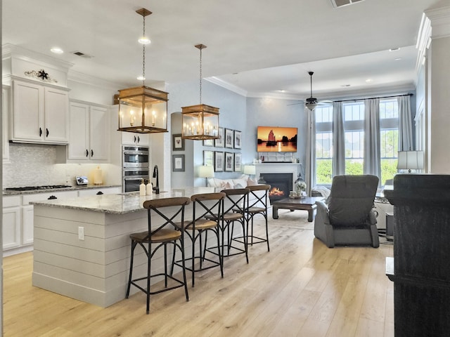 kitchen with ceiling fan with notable chandelier, double oven, light wood-style floors, and ornamental molding