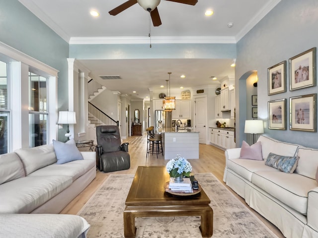 living area with a ceiling fan, visible vents, light wood finished floors, arched walkways, and crown molding