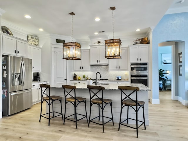 kitchen with backsplash, ornamental molding, arched walkways, stainless steel appliances, and a sink