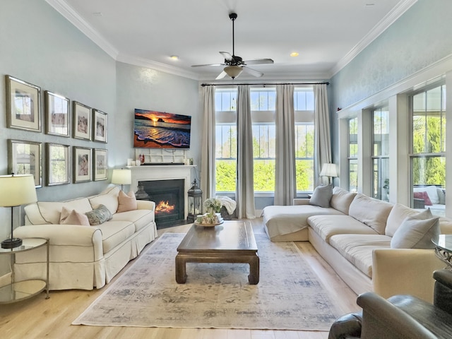 living room with a warm lit fireplace, crown molding, a ceiling fan, and wood finished floors