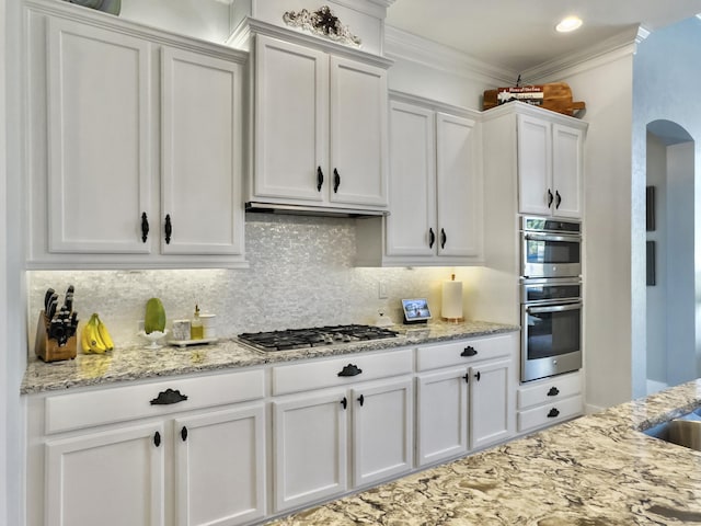 kitchen with arched walkways, ornamental molding, decorative backsplash, stainless steel appliances, and white cabinets