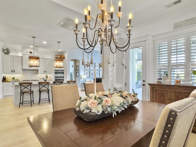 dining space with light wood-type flooring, visible vents, a notable chandelier, and crown molding