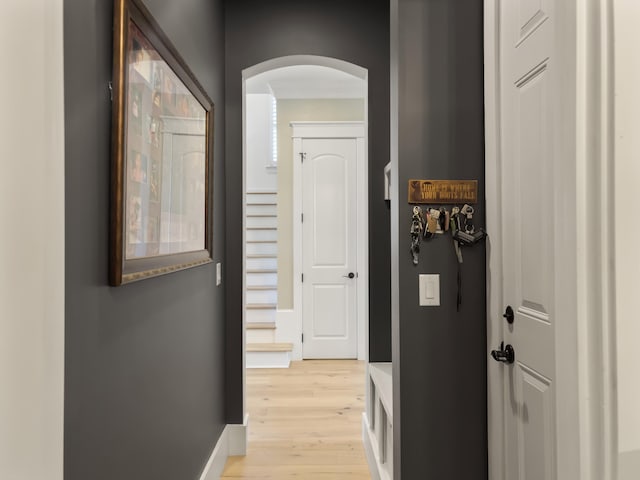 hallway featuring baseboards, arched walkways, and light wood-type flooring