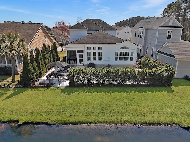 rear view of property featuring fence, roof with shingles, a yard, a sunroom, and a patio area