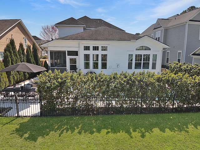 rear view of property featuring fence, a lawn, a shingled roof, and a sunroom