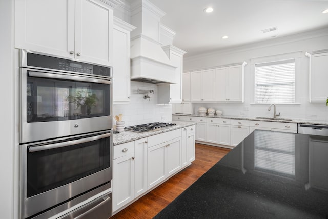 kitchen with sink, appliances with stainless steel finishes, light stone counters, white cabinets, and dark hardwood / wood-style flooring