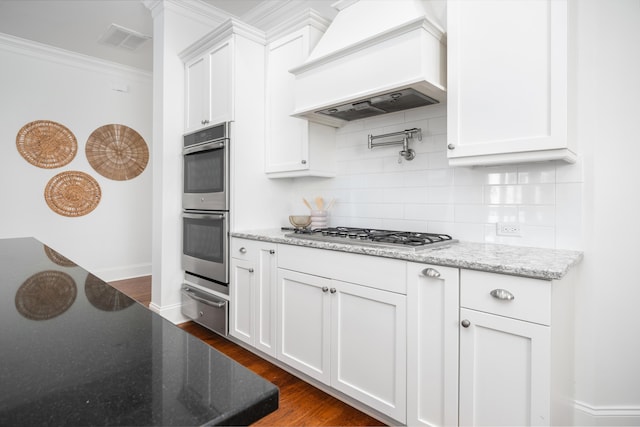 kitchen featuring stainless steel appliances, light stone countertops, custom range hood, and white cabinets