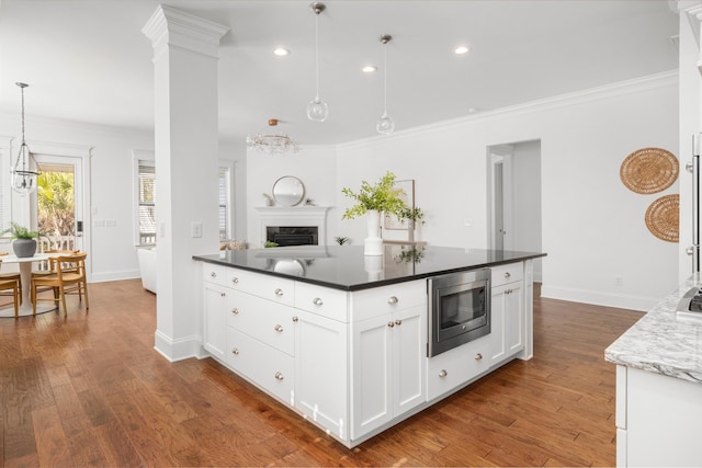 kitchen with stainless steel microwave, white cabinets, hanging light fixtures, crown molding, and dark wood-type flooring