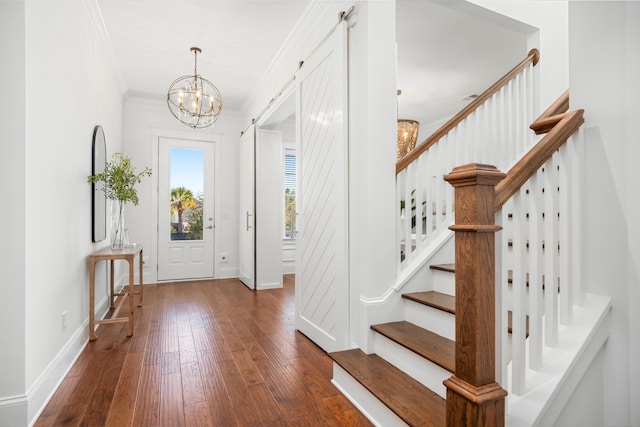 entryway with dark hardwood / wood-style floors, ornamental molding, a barn door, and a chandelier