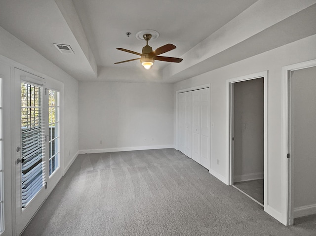 unfurnished bedroom featuring a raised ceiling, ceiling fan, and carpet flooring