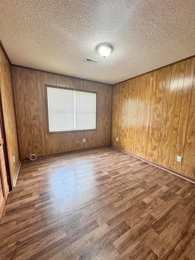 spare room featuring wood walls, a textured ceiling, and hardwood / wood-style flooring