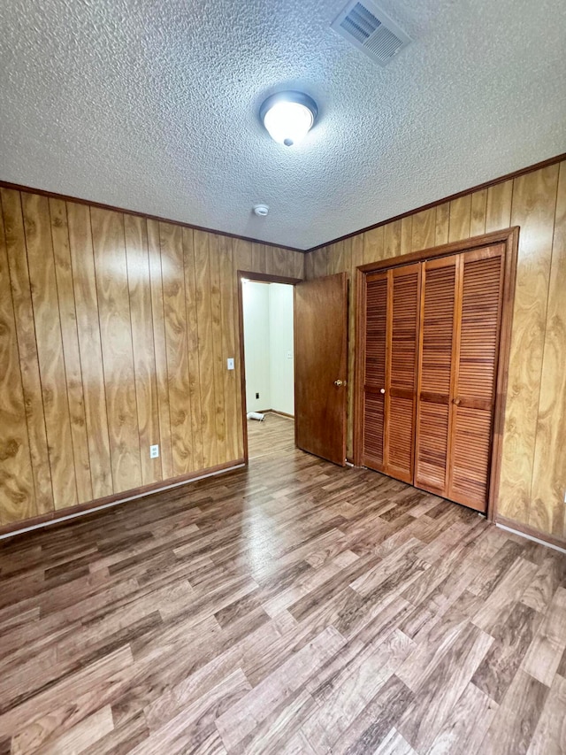 unfurnished bedroom featuring hardwood / wood-style floors, a textured ceiling, and wooden walls