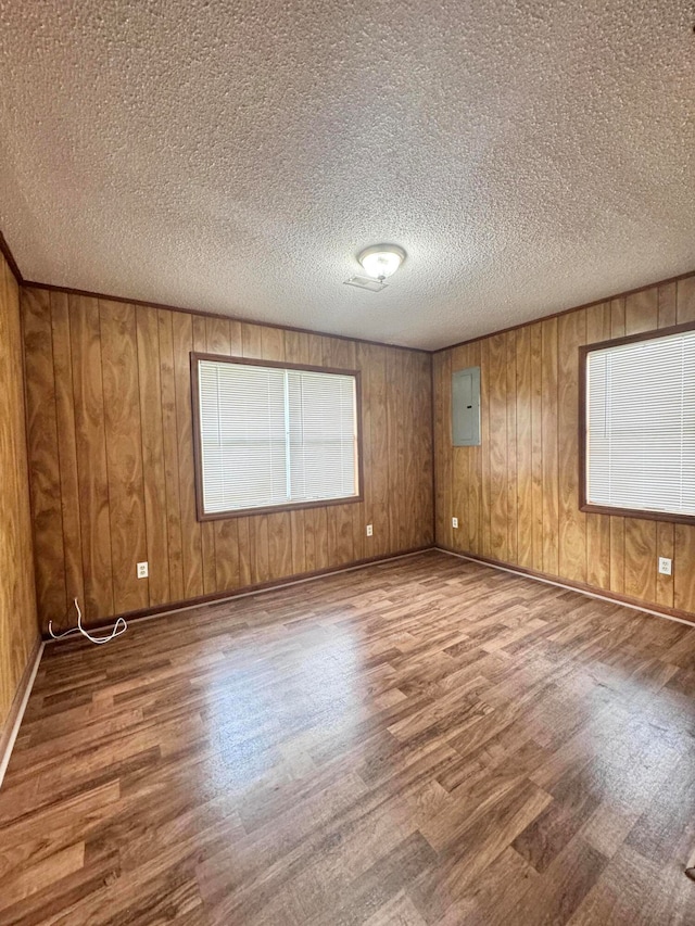 empty room with wood walls, a textured ceiling, electric panel, and hardwood / wood-style flooring