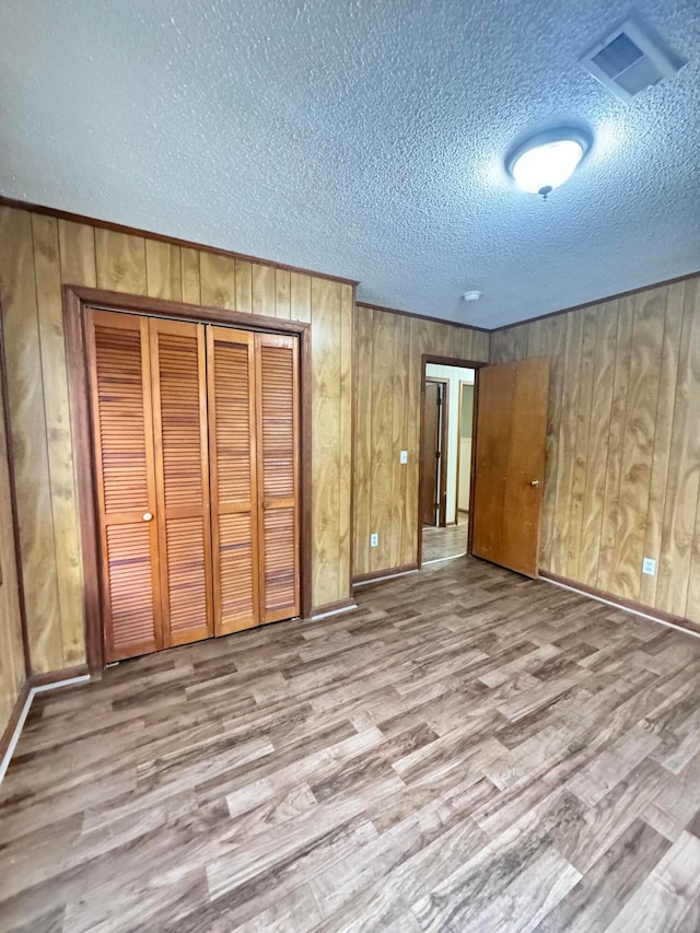 unfurnished bedroom featuring wood walls, light hardwood / wood-style flooring, a textured ceiling, and a closet