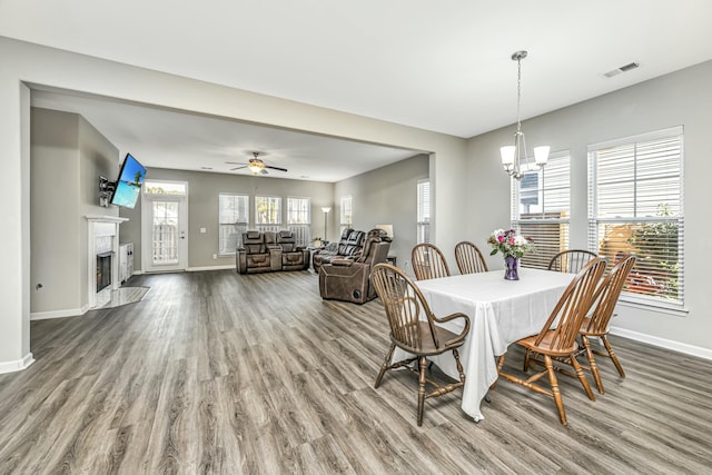 dining area featuring wood-type flooring, ceiling fan with notable chandelier, and a premium fireplace