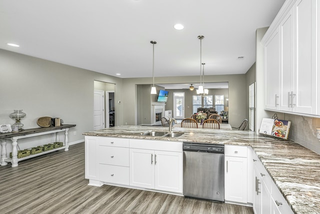 kitchen with kitchen peninsula, stainless steel dishwasher, sink, white cabinets, and light stone countertops