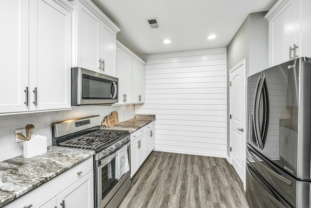 kitchen featuring light stone countertops, hardwood / wood-style flooring, white cabinetry, wooden walls, and stainless steel appliances