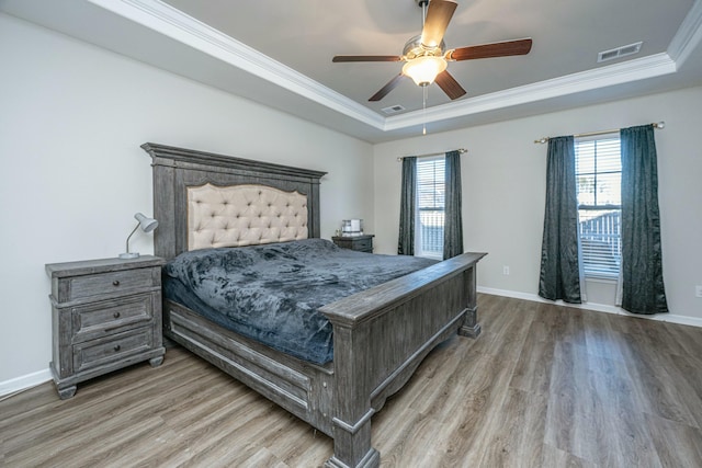 bedroom with ceiling fan, a raised ceiling, crown molding, and hardwood / wood-style flooring