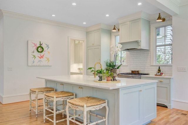 62 Eastlake Rd, Mount Pleasant, SC 29464 - kitchen featuring light wood-style flooring, tasteful backsplash, a kitchen breakfast bar, ornamental molding, and an island with sink