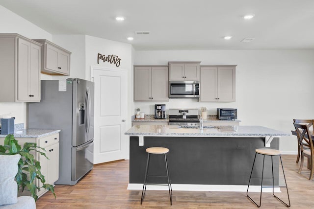 kitchen featuring a breakfast bar area, light stone counters, gray cabinets, appliances with stainless steel finishes, and light wood-style flooring