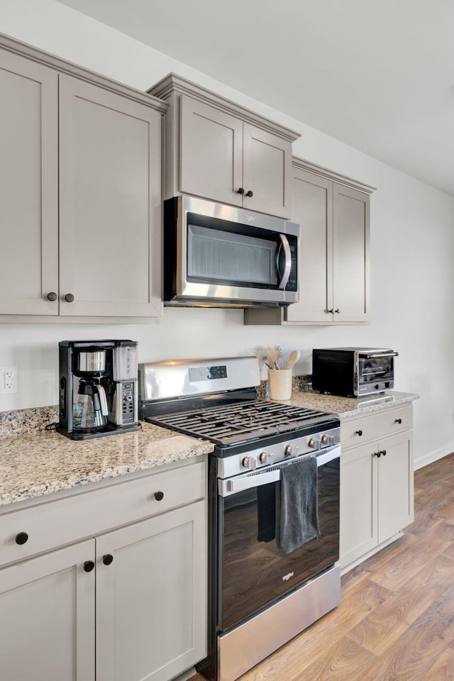 kitchen featuring light wood-type flooring, gray cabinetry, appliances with stainless steel finishes, a toaster, and light stone countertops