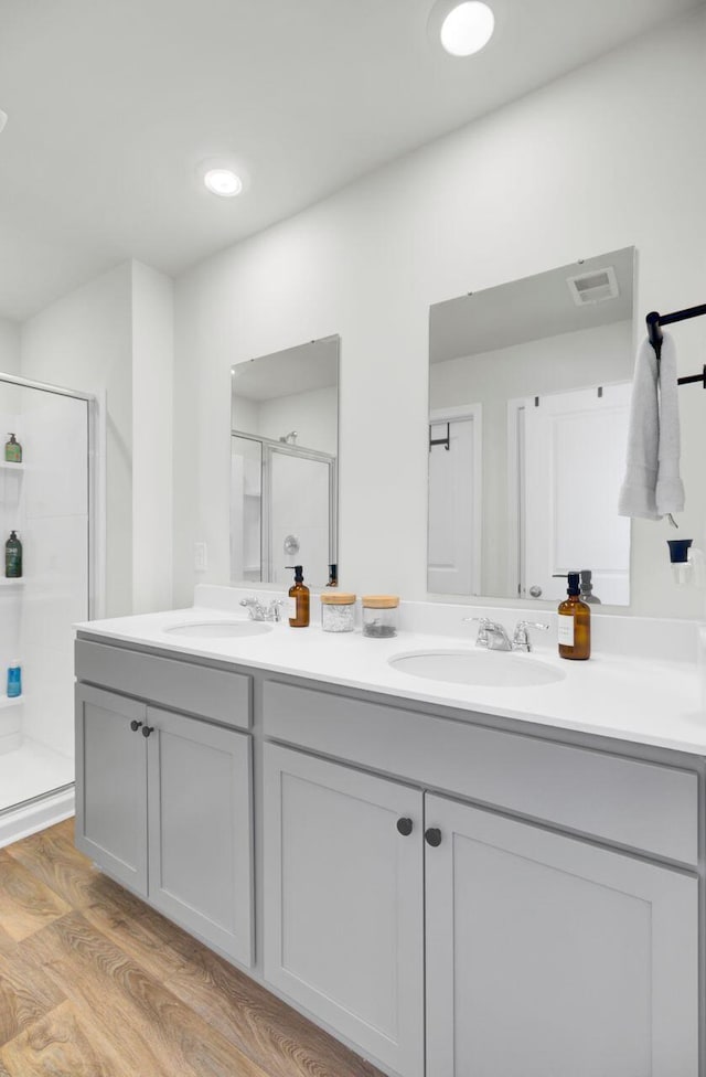 full bathroom with double vanity, wood finished floors, a stall shower, and a sink