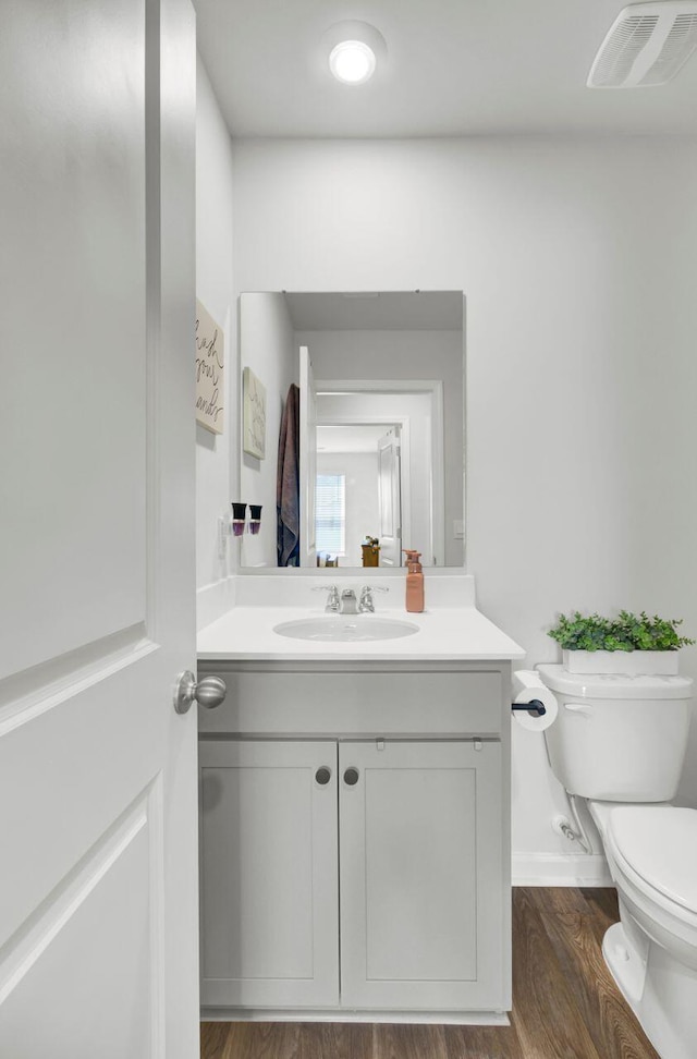 half bath featuring vanity, toilet, wood finished floors, and visible vents