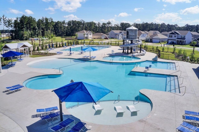 pool with a hot tub, a water slide, fence, a residential view, and a patio area