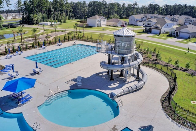 community pool featuring a patio, fence, a water slide, a yard, and a residential view