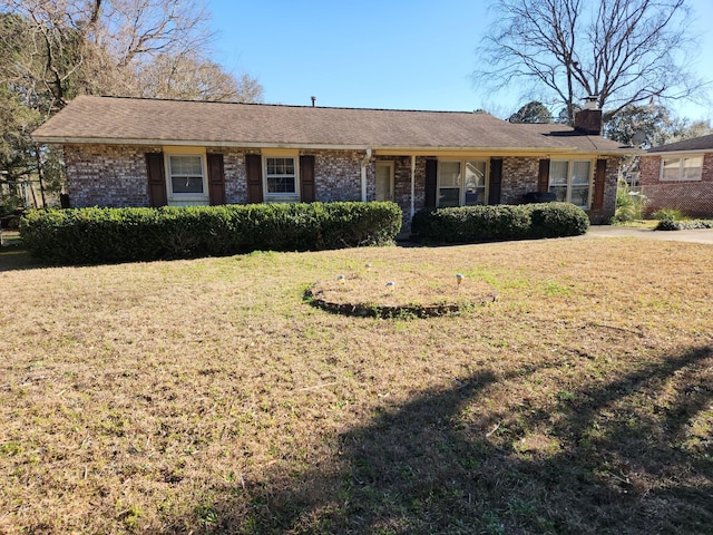 ranch-style house featuring brick siding, a chimney, and a front lawn