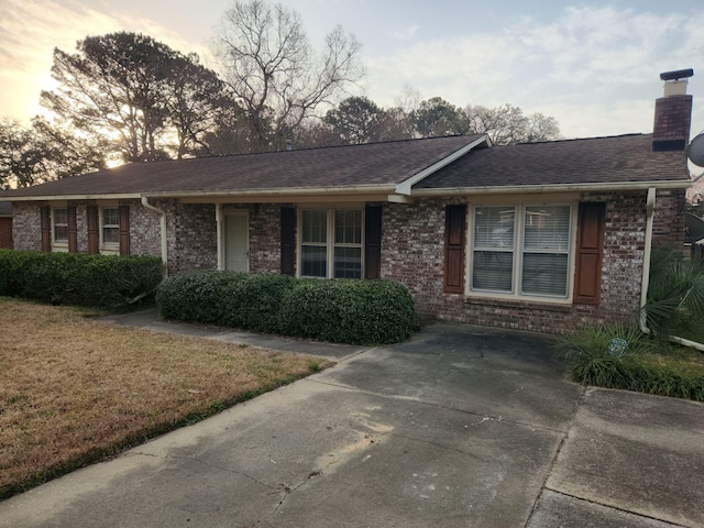 ranch-style house with a front yard, roof with shingles, a chimney, and brick siding